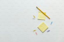 A white table topped with yellow sticky notes, paperclips and a pencil